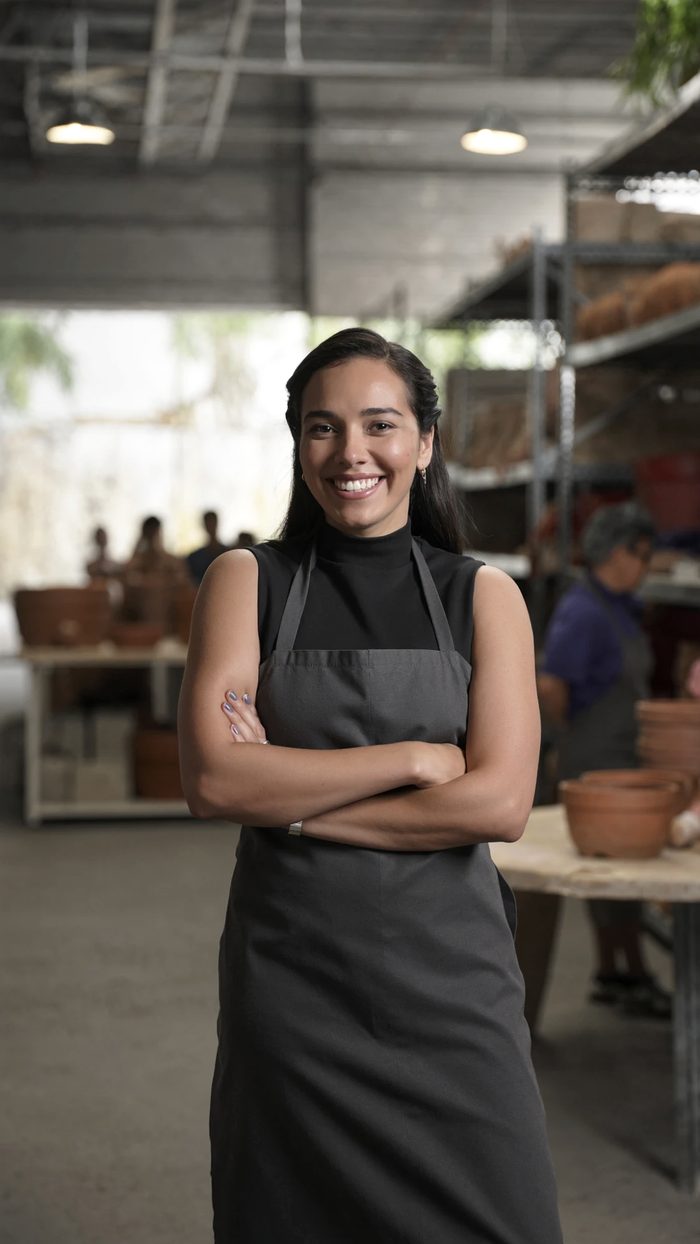 Imagen ilustrativa: emprendedora sonriente, de brazos cruzados, en su taller de cerámica