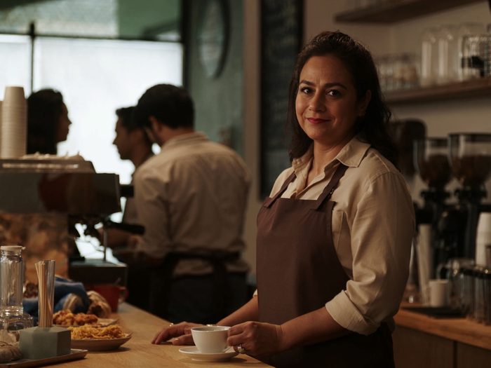 Imagen ilustrativa: dueña de una cafetería, sonriente detrás de su mostrador