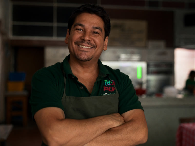 Imagen ilustrativa: dueño de un restaurante, sonriente y de brazos cruzados, dentro de su local